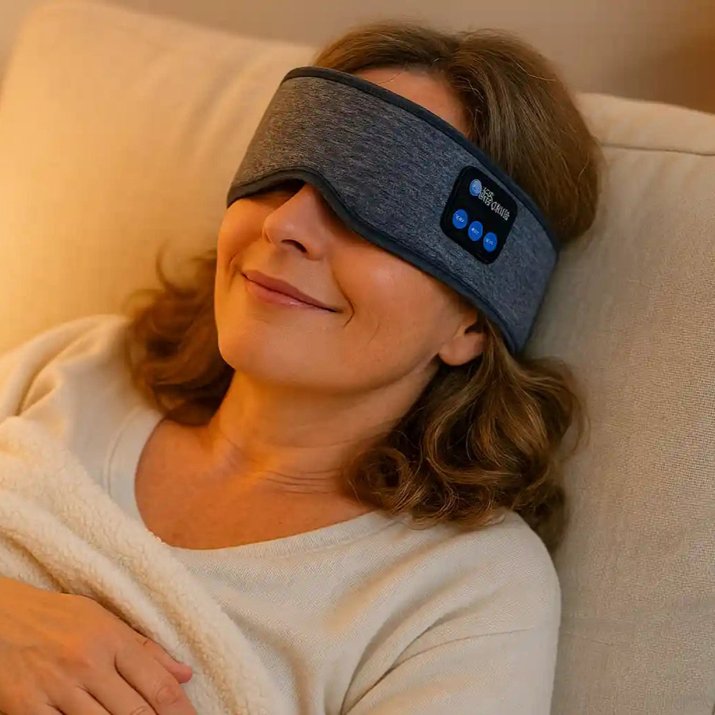 Femme souriante et détendue dormant sur un canapé avec le bandeau de sommeil SleepBand™ sur les yeux, illustrant le confort nocturne.