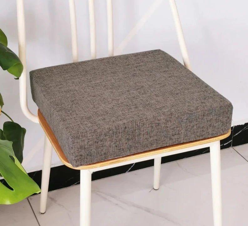 Coussin carré épais gris foncé posé sur une chaise à structure blanche