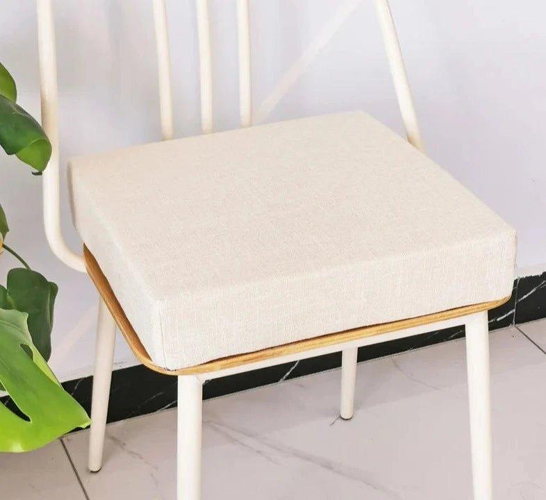 Coussin carré épais beige posé sur une chaise à structure blanche
